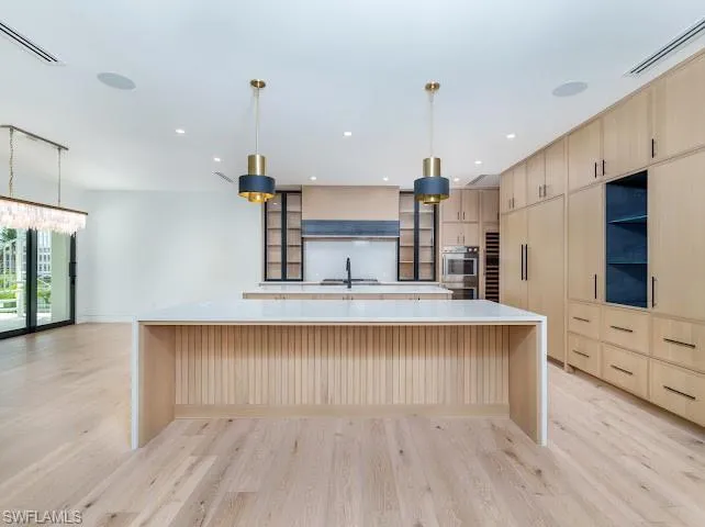 Kitchen featuring light wood finish cabinetry, hanging light fixtures, light wood-type flooring, and light stone countertops