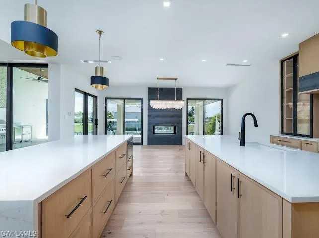 Kitchen featuring a large island, pendant lighting, light stone countertops, light wood-style flooring, and glass fronted cabinets