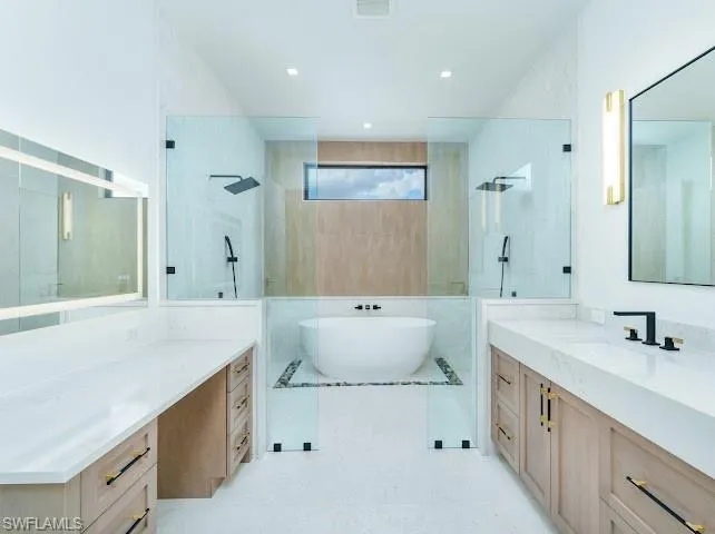 Bathroom with walk in shower, two vanities, and a soaking tub