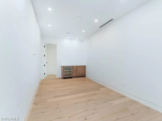 Empty room featuring light wood-style flooring, wine cooler, recessed lighting, and bar area