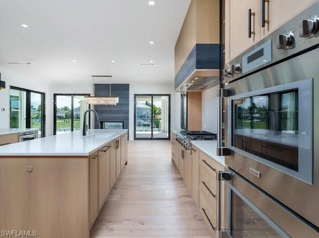 Kitchen featuring stainless steel appliances, a large island, light wood finished floors, light stone counters, and hanging light fixtures