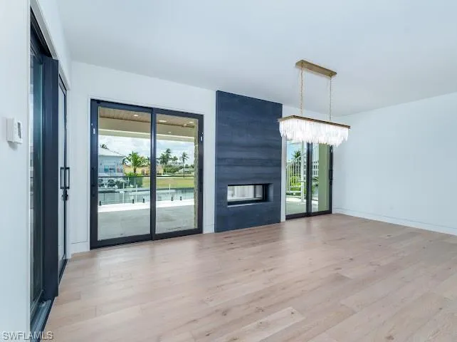 Unfurnished living room featuring light wood-style flooring, healthy amount of natural light, a large fireplace, and a chandelier