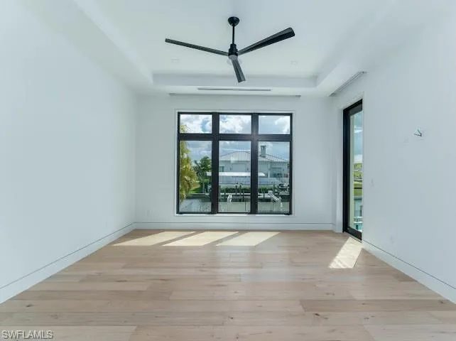 Empty room with light wood-type flooring, a ceiling fan, and a raised ceiling