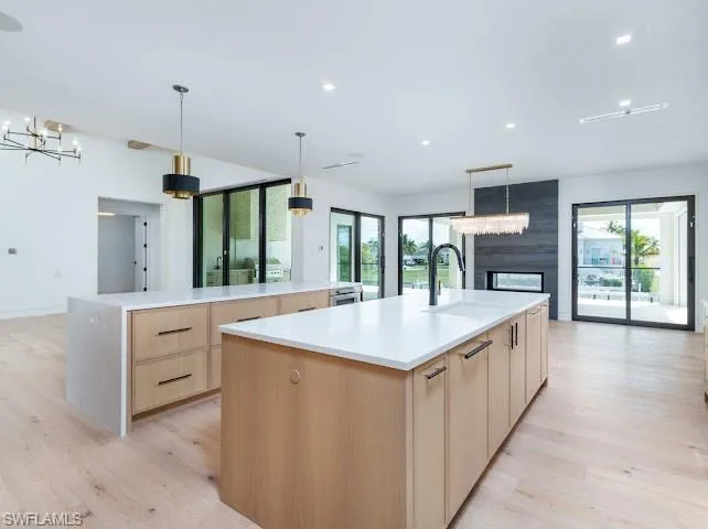 Kitchen with light wood finish cabinetry, suspended lighting, open floor plan, light wood finished floors, and plenty of natural light