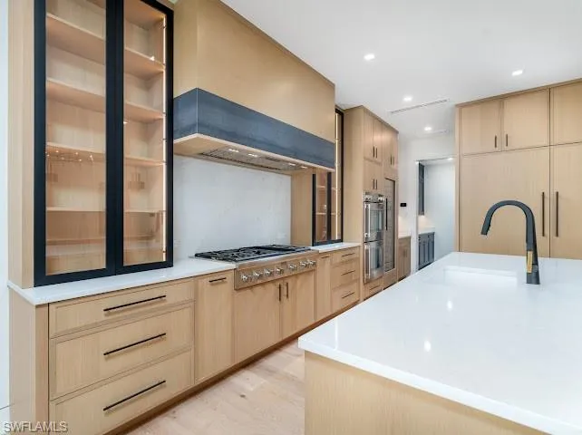 Kitchen featuring light wood finish cabinetry, light wood-style floors, recessed lighting, stainless steel appliances, and light stone counters