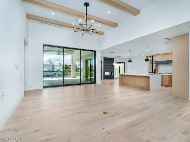 Unfurnished living room with hanging lights, plenty of natural light, and light wood-style floors