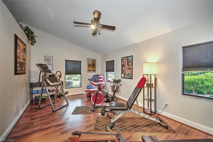 Exercise room featuring a textured ceiling, hardwood / wood-style flooring, vaulted ceiling, and ceiling fan