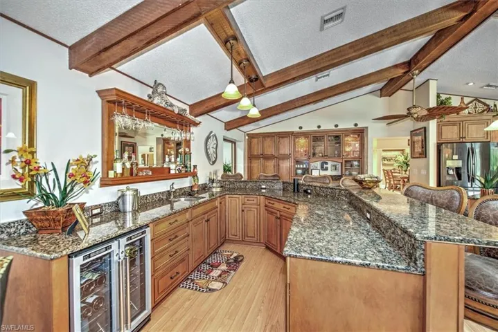 Kitchen with dark stone countertops, a textured ceiling, light hardwood / wood-style floors, lofted ceiling with beams, and stainless steel refrigerator with ice dispenser
