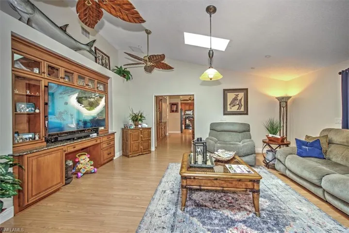 Living room featuring light hardwood / wood-style floors, high vaulted ceiling, ceiling fan, and a skylight