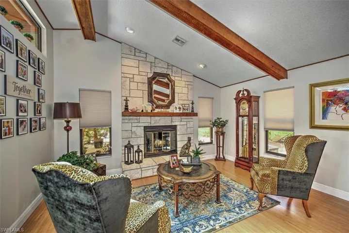 Living room with lofted ceiling with beams, a textured ceiling, a stone fireplace, and light wood-type flooring