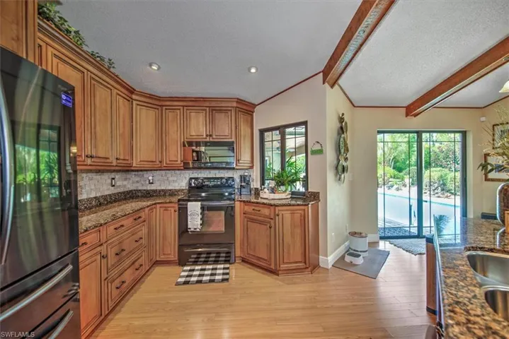 Kitchen featuring dark stone counters, black appliances, backsplash, light hardwood / wood-style floors, and a textured ceiling
