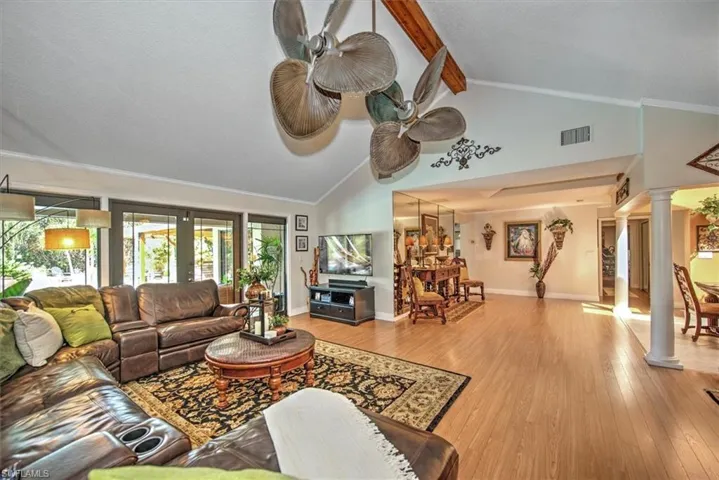 Living room with beam ceiling, crown molding, light hardwood / wood-style flooring, ornate columns, and high vaulted ceiling