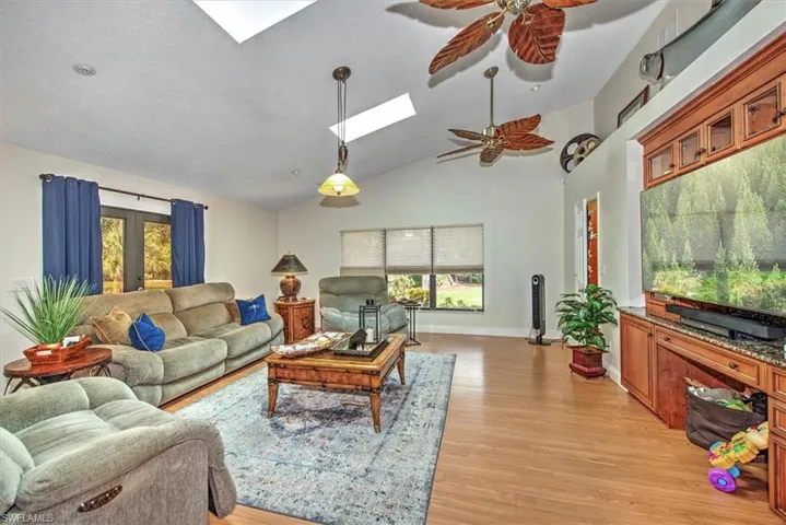 Living room featuring light hardwood / wood-style floors, vaulted ceiling with skylight, ceiling fan, and french doors