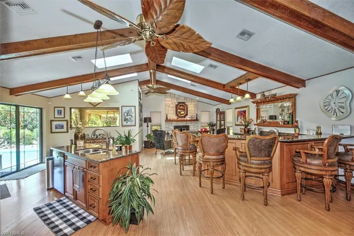 Kitchen featuring dark stone counters, sink, light hardwood / wood-style floors, lofted ceiling with skylight, and ceiling fan