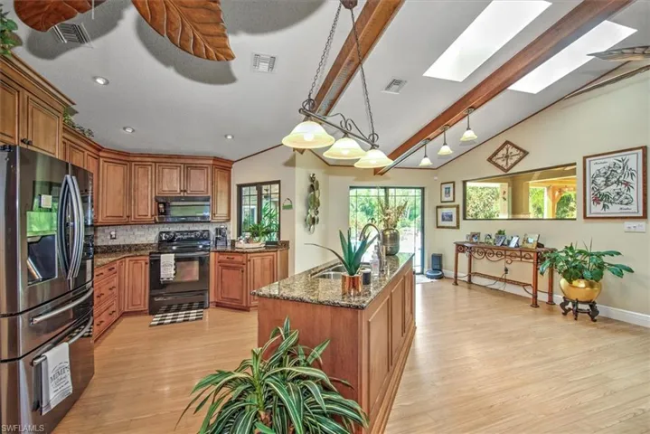 Kitchen with dark stone counters, black appliances, hanging light fixtures, lofted ceiling with skylight, and light wood-type flooring