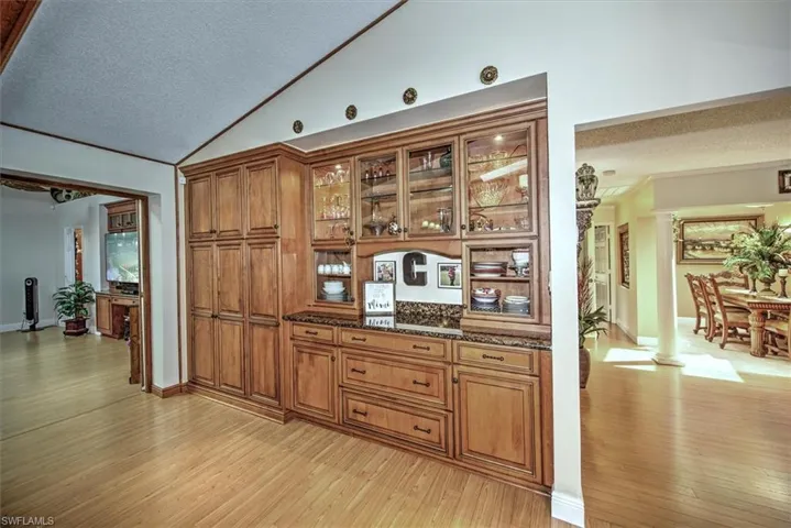 Bar featuring dark stone countertops, light wood-type flooring, lofted ceiling, and a textured ceiling