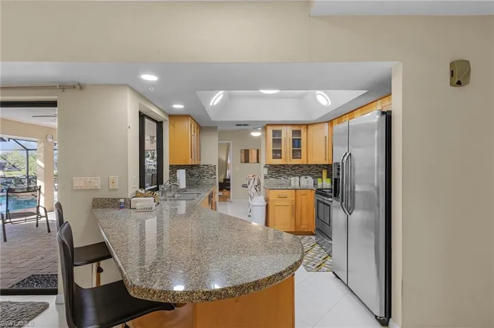 Kitchen featuring kitchen peninsula, appliances with stainless steel finishes, a kitchen bar, decorative backsplash, and a raised ceiling