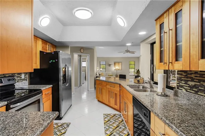 Kitchen with ceiling fan, sink, stainless steel appliances, a raised ceiling, and dark stone countertops