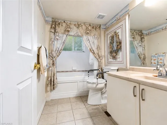 Bathroom featuring a white panel door, tiled flooring, a bathtub with a white tiled surround, and a vanity with a light-colored countertop and integrated sink