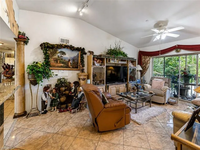 Living area featuring vaulted ceilings, track lighting, ceiling fan, tile flooring, and sliding glass door access to an exterior balcony