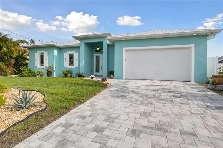 The front of the house features a welcoming design with a wide paver driveway, lush landscaping, and a charming entryway.