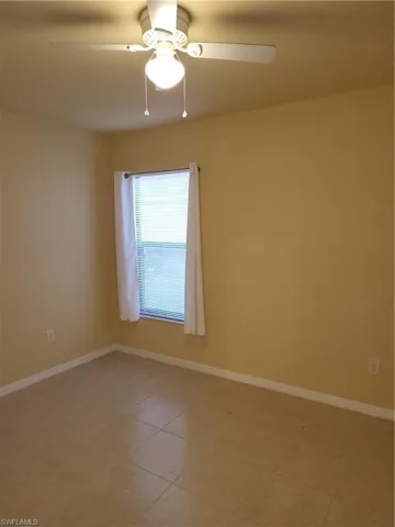 Spare room featuring light tile patterned flooring, a ceiling fan, and baseboards