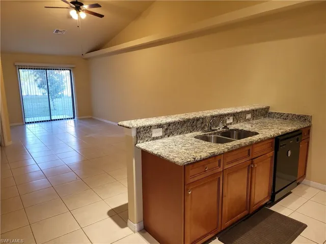 Kitchen featuring black dishwasher, brown cabinetry, vaulted ceiling, a sink, and light tile patterned flooring