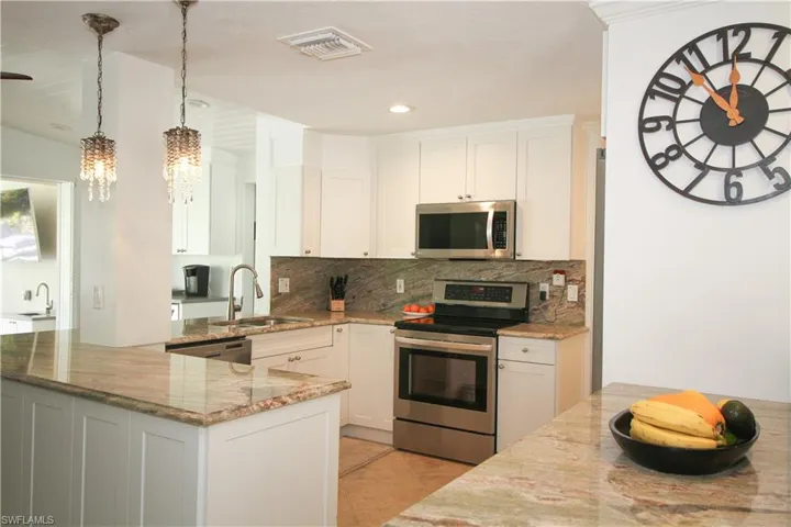 Kitchen with stainless steel appliances, white cabinets, light stone countertops, decorative light fixtures, and recessed lighting