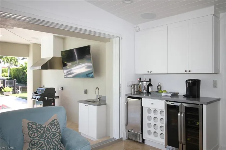 Indoor wet bar with beverage cooler, dark countertops, white cabinetry, stainless steel fridge, and light tile patterned floors