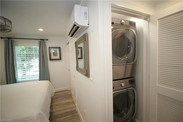 Laundry area with ornamental molding, stacked washer / dryer, an AC wall unit, dark wood-style floors, and recessed lighting