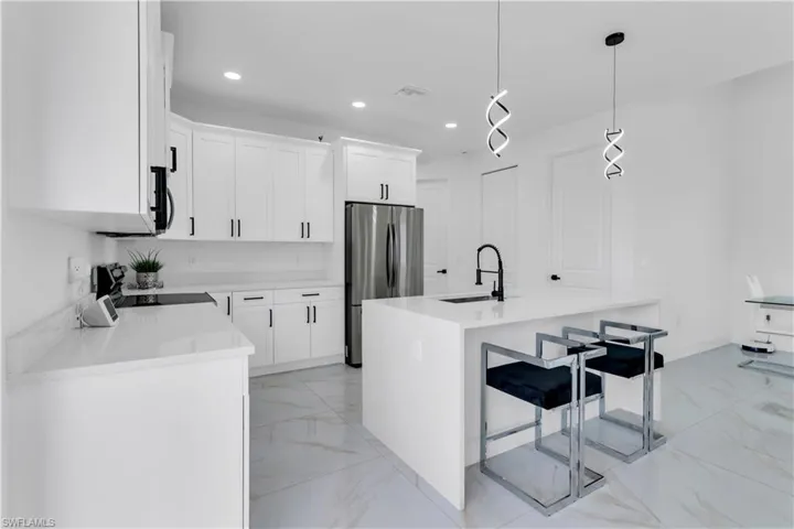 Kitchen with stainless steel appliances, sink, hanging light fixtures, an island with sink, and light tile patterned flooring