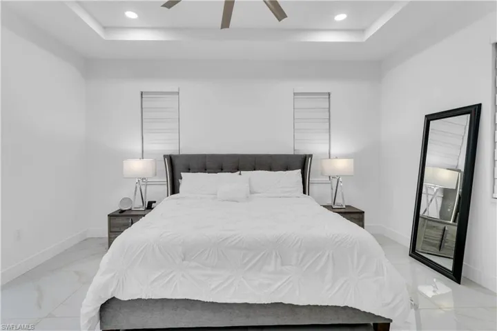Tiled bedroom featuring a tray ceiling and ceiling fan