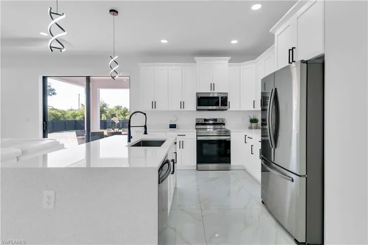 Kitchen with white cabinetry, stainless steel appliances, pendant lighting, sink, and light tile patterned floors
