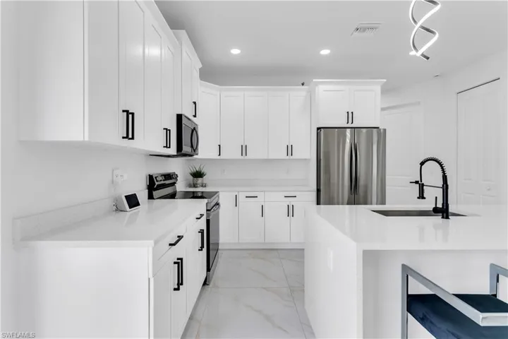 Kitchen with sink, appliances with stainless steel finishes, white cabinets, and light tile patterned floors