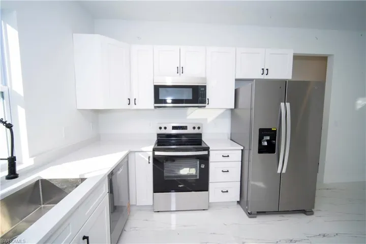 Kitchen with stainless steel appliances, white cabinets, light stone counters, and light marble finish floors