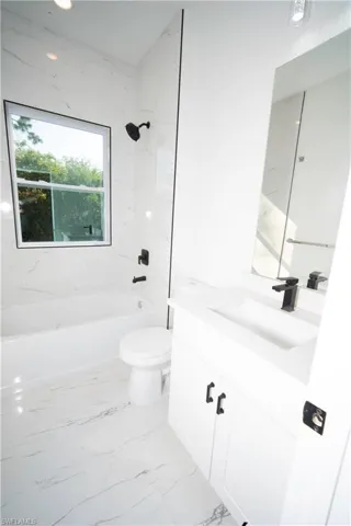 Bathroom featuring bathing tub / shower combination, vanity, and light marble finish flooring