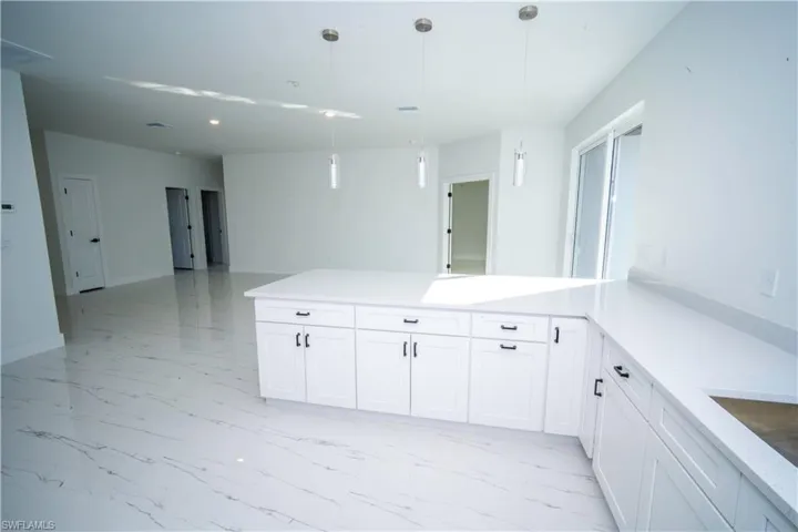 Kitchen with decorative light fixtures, light marble finish flooring, a peninsula, and white cabinetry
