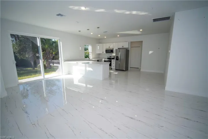 Kitchen with white cabinetry, stainless steel appliances, decorative light fixtures, open floor plan, and light marble finish floors