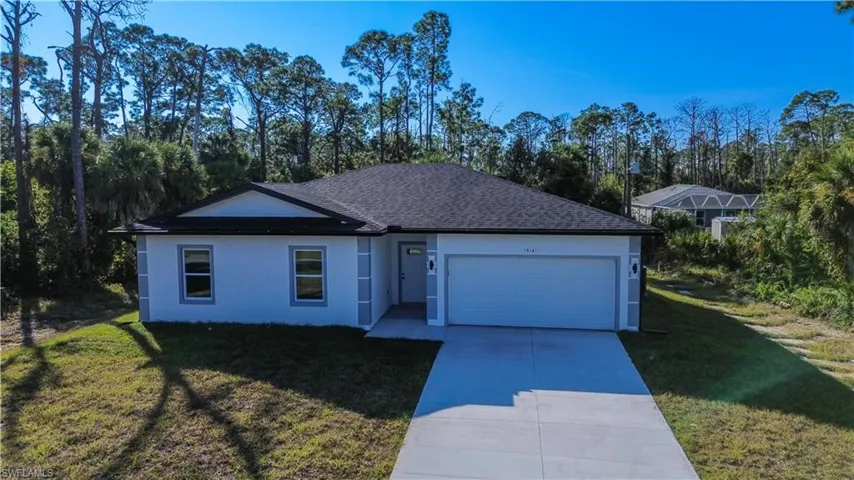 Single story home featuring a front lawn, driveway, stucco siding, an attached garage, and view of scattered trees