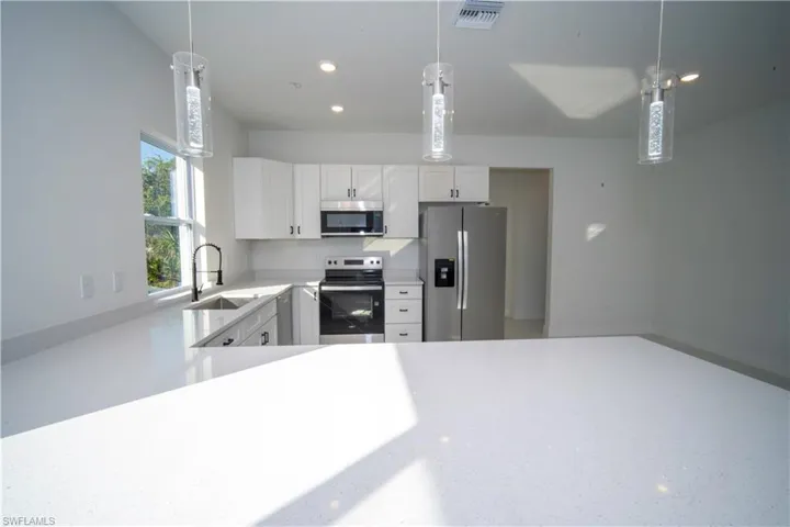 Kitchen with stainless steel appliances, white cabinetry, decorative light fixtures, light stone countertops, and recessed lighting