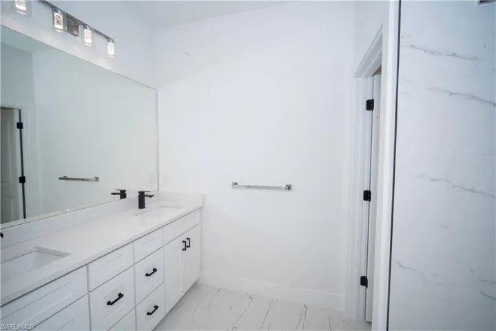 Full bath featuring double vanity and light marble finish floors