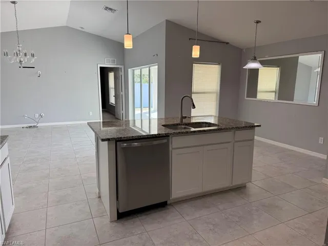 Kitchen featuring light tile patterned flooring, stainless steel dishwasher, dark stone counters, an island with sink, and lofted ceiling