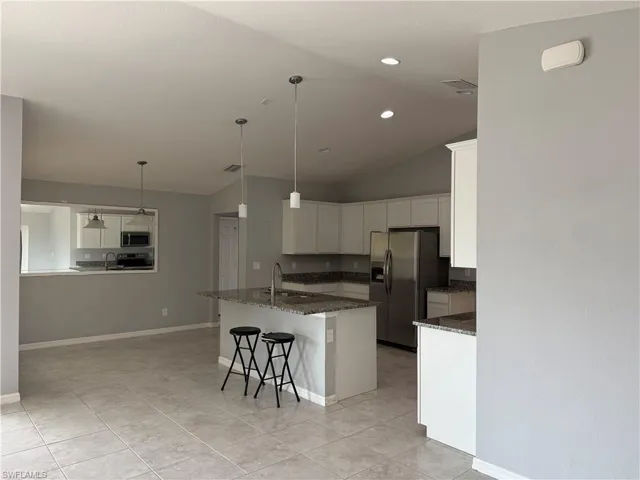 Kitchen with a breakfast bar, white cabinetry, dark stone counters, stainless steel appliances, and vaulted ceiling