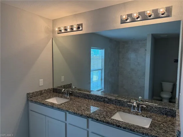 Full bath with a textured wall, double vanity, and tiled shower