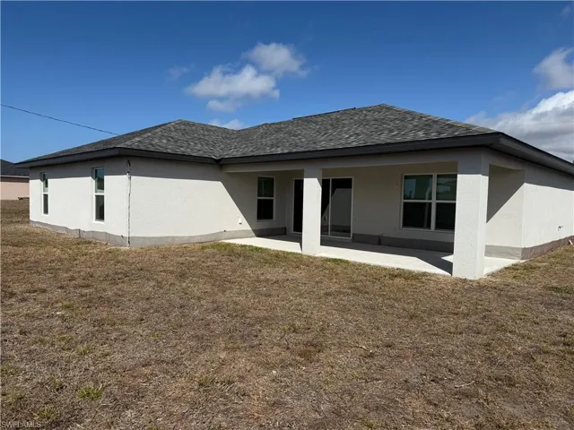 Back of house featuring a lawn, a patio area, and a shingled roof