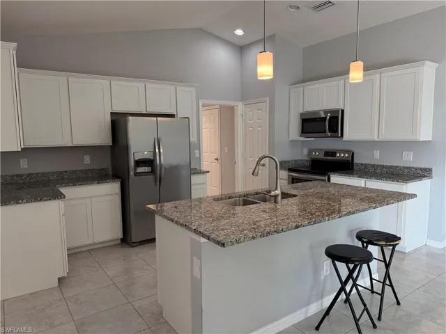 Kitchen with stainless steel appliances, white cabinets, dark stone countertops, light tile patterned floors, and hanging light fixtures