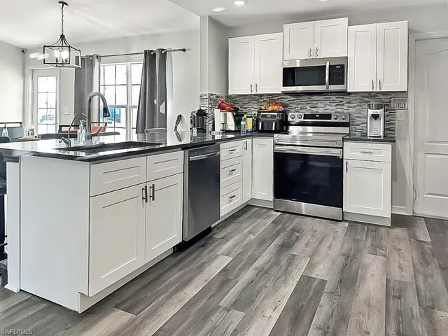 Kitchen with white cabinetry, stainless steel appliances, a peninsula, and backsplash