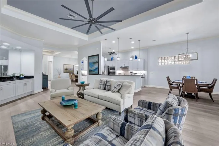 Living area with a raised ceiling, crown molding, new light vinyl planked floors, a chandelier, and recessed lighting