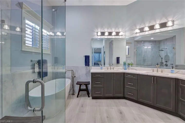 Full bathroom featuring a freestanding tub, a shower stall, double vanity, a wainscoted wall, tile flooring and tile walls