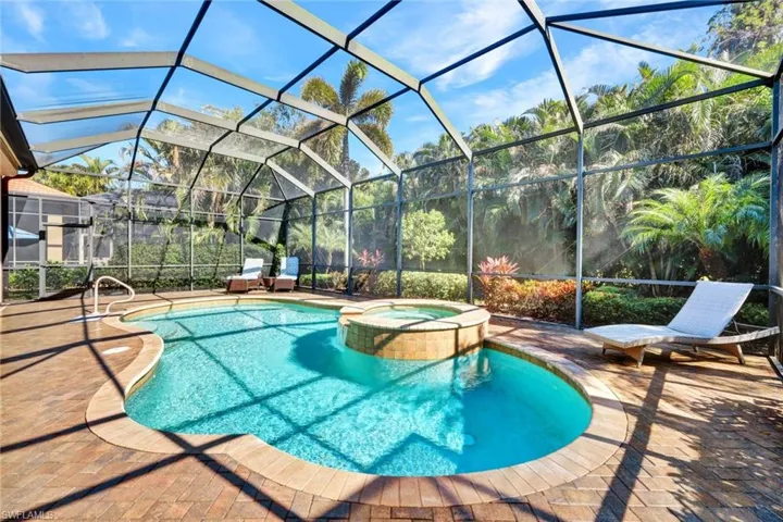 View of swimming pool featuring a pool with connected hot tub, screened in lanai, and a patio area